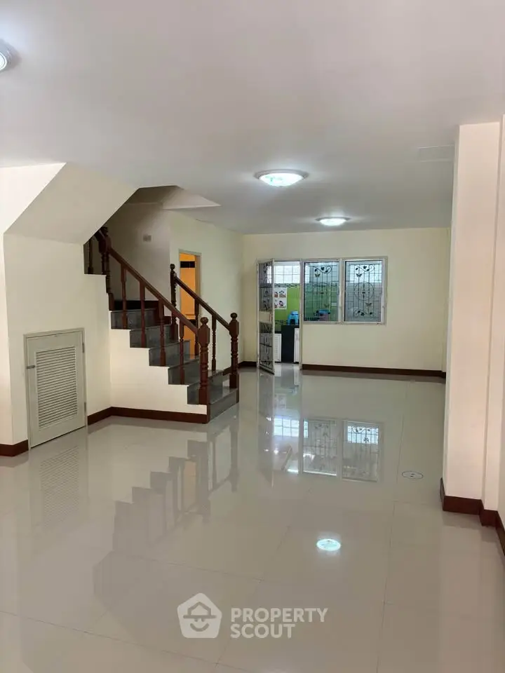 Spacious living room with glossy tiled floors and elegant staircase in modern home.