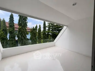 Spacious modern balcony with sleek glass railing and lush greenery view.
