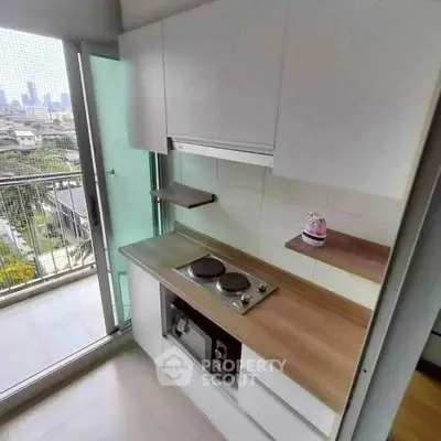 Modern compact kitchen with electric stove and balcony view in urban apartment.
