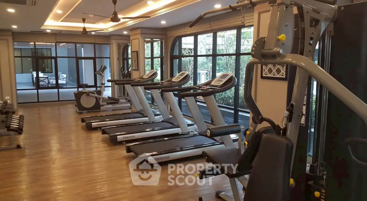 Spacious gym with modern equipment and large windows in luxury residential building.