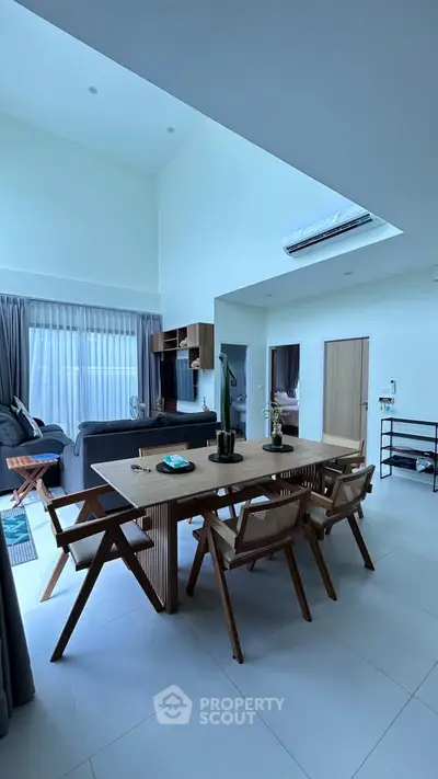 Spacious modern living room with high ceiling and elegant dining area, featuring stylish wooden furniture and natural light.