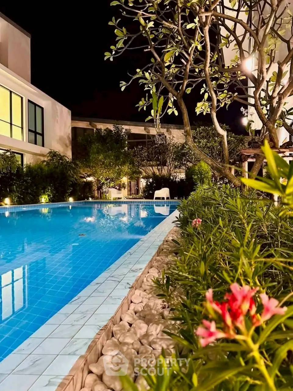Luxurious night view of a serene poolside with lush greenery and modern architecture.