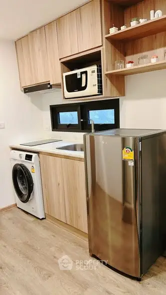 Modern kitchen with wooden cabinets, washing machine, microwave, and fridge.