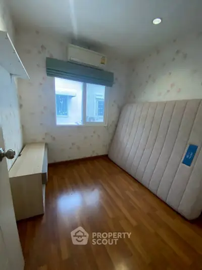 Cozy bedroom with wooden flooring and natural light, featuring an air conditioner and a large window.