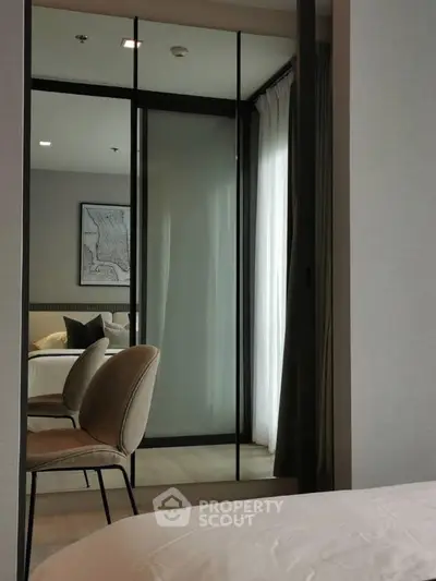 Modern bedroom with stylish decor and mirrored wardrobe reflecting natural light.