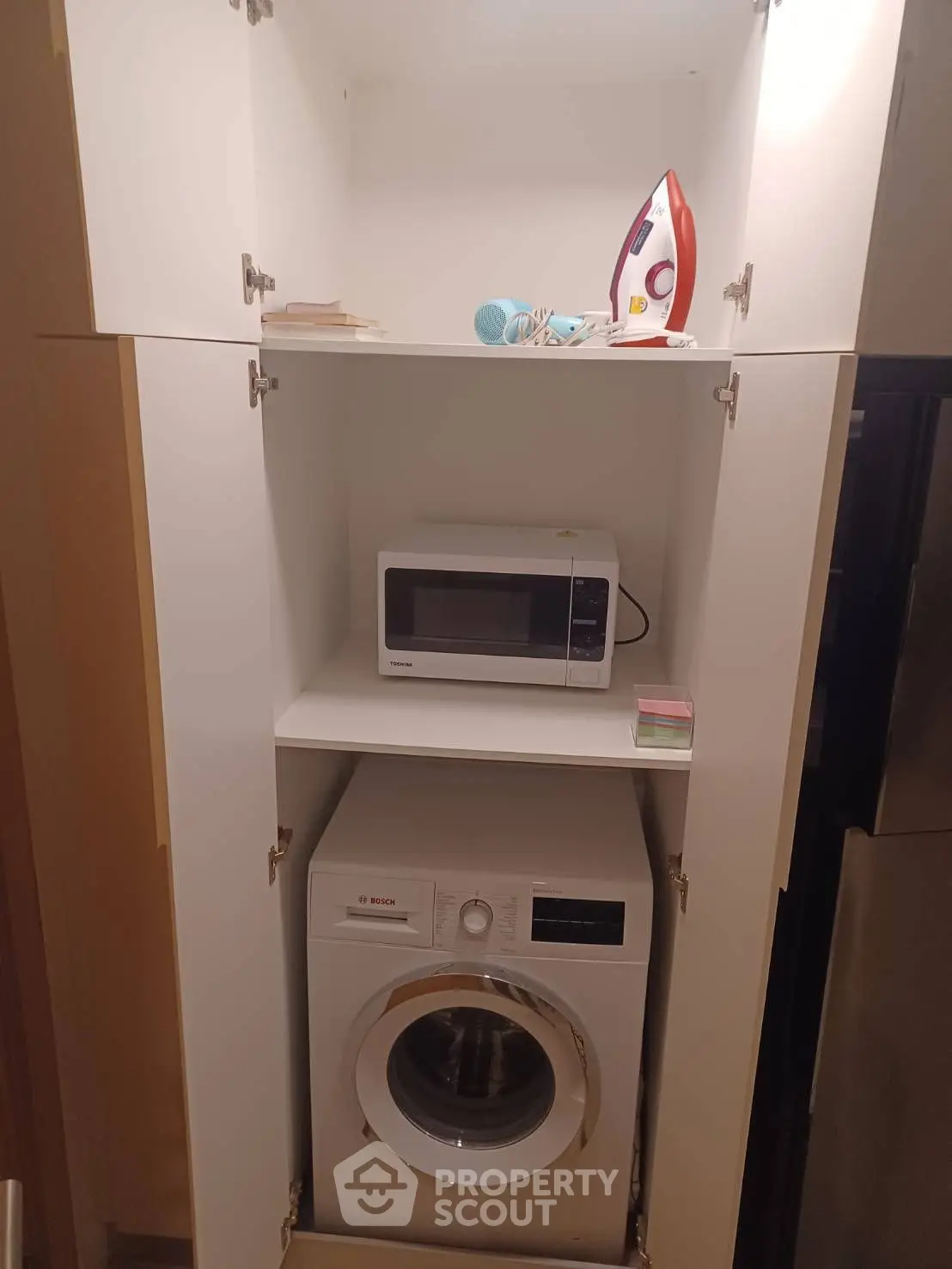 Compact laundry and kitchen appliance setup with washing machine, microwave, and iron in a cabinet.