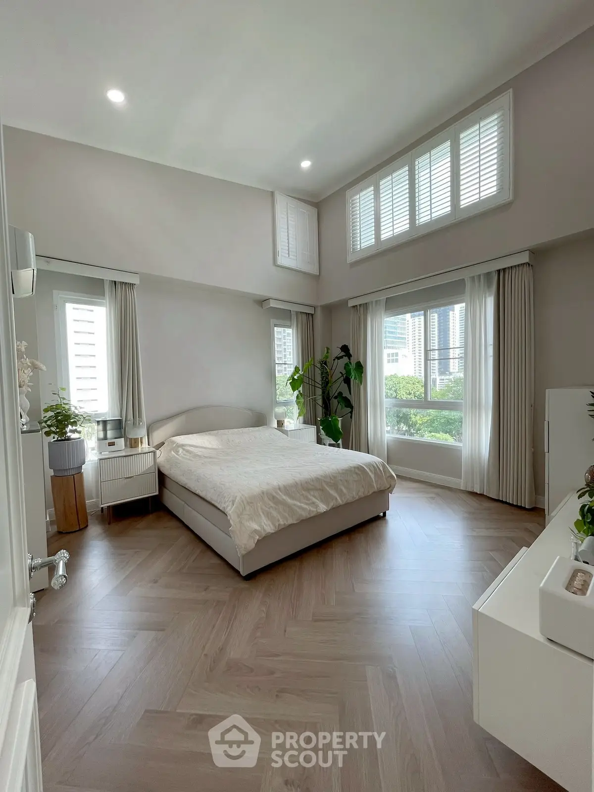 Spacious bedroom with large windows and modern decor, offering a serene and airy atmosphere.