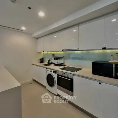 Modern kitchen with sleek white cabinets, built-in oven, and washing machine in a contemporary apartment.