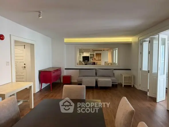 Spacious living room with modern furniture and wooden flooring, featuring a large mirror and ample natural light.