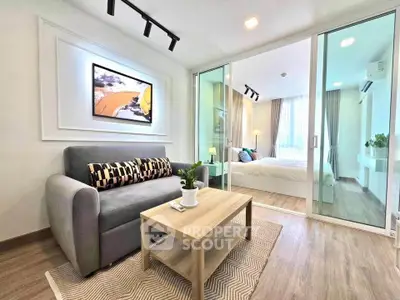 Modern living room with cozy sofa and stylish decor leading to a bright bedroom through glass doors.