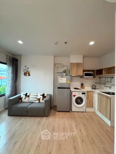 Modern open-layout living room with kitchen, featuring a cozy sofa, washing machine, and stylish decor.