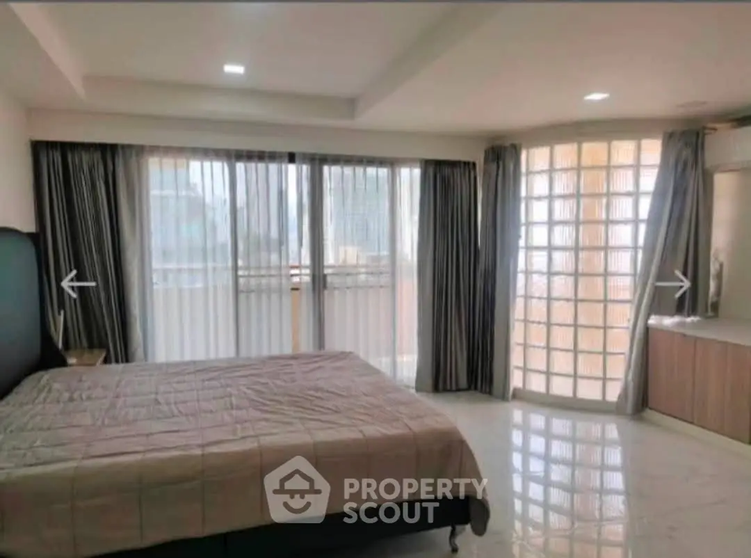 Spacious bedroom with large windows and modern decor in a high-rise apartment.