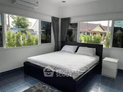 Cozy bedroom with large windows and modern furnishings in a serene residential area.