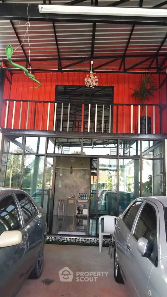 Modern carport with vibrant red facade and glass doors, featuring parked cars and stylish overhead lighting.