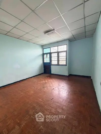 Spacious empty room with parquet flooring and large window, ideal for customization.