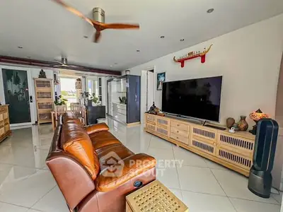 Spacious living room with leather sofa and large TV, featuring modern decor and ceiling fan.