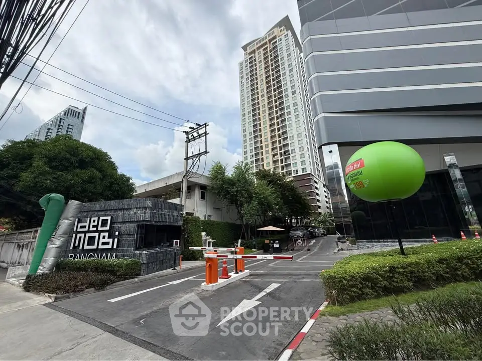 Modern high-rise condominium entrance with lush greenery and secure access in vibrant urban setting.