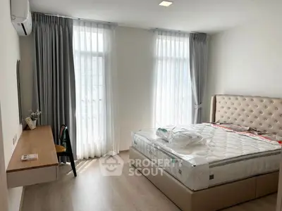 Modern bedroom with large windows, stylish bed, and sleek desk in a bright, airy space.