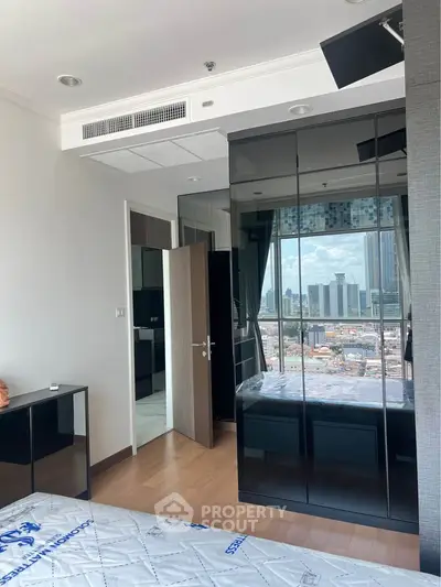 Modern bedroom with city view, featuring sleek black wardrobe and wooden flooring.
