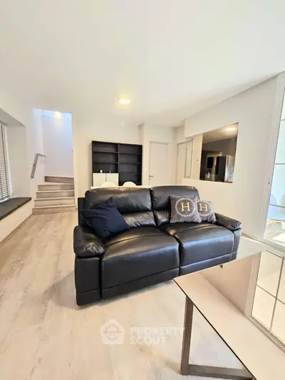 Modern living room with sleek black leather sofa and open kitchen layout