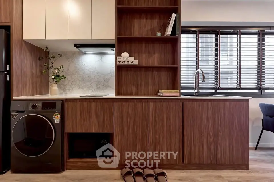 Modern kitchen with sleek wooden cabinets and built-in appliances, featuring a washing machine and stylish decor.