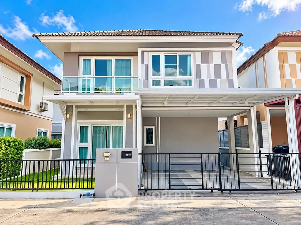 Modern two-story house with balcony and gated driveway in a suburban neighborhood.