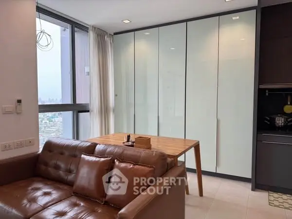 Modern living room with leather sofa and dining table near large window with city view.