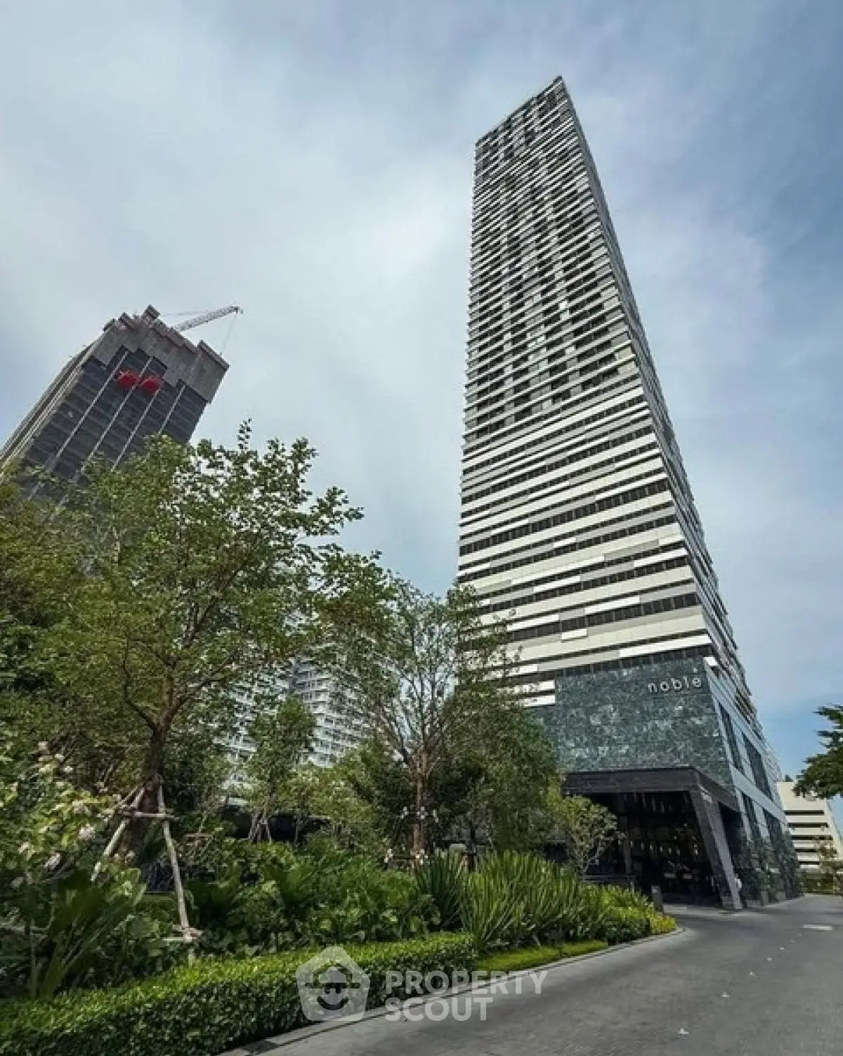 Stunning high-rise building with modern architecture and lush greenery at the entrance.