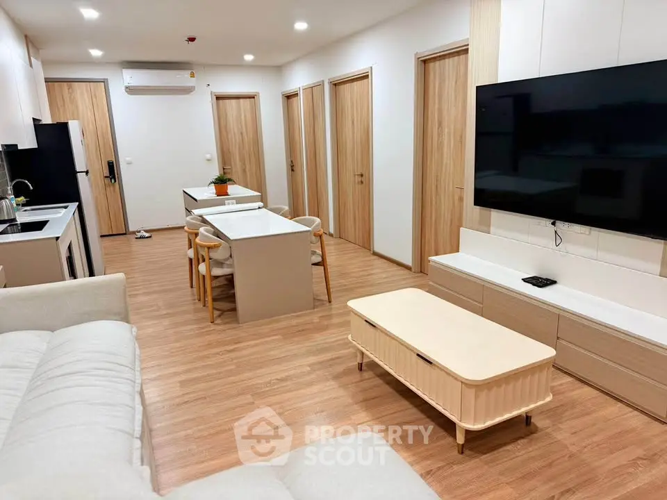 Modern open-plan living room with sleek kitchen and dining area, featuring a large wall-mounted TV and stylish furniture.