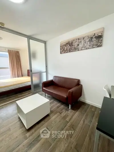 Modern living room with brown sofa and cityscape artwork, featuring sliding glass doors to bedroom.