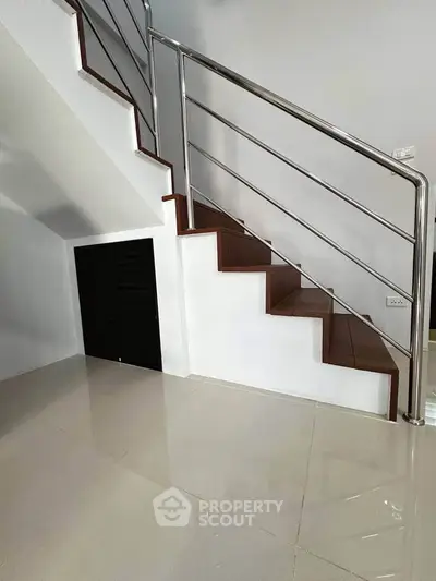 Modern staircase with sleek metal railing and glossy tiled flooring in a contemporary home interior.