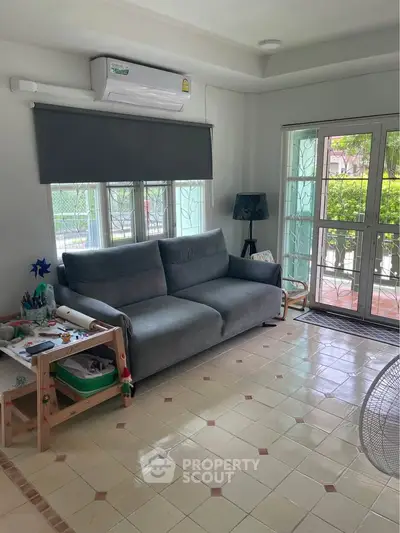 Charming living room with cozy sofa, air conditioning, and natural light from large windows.