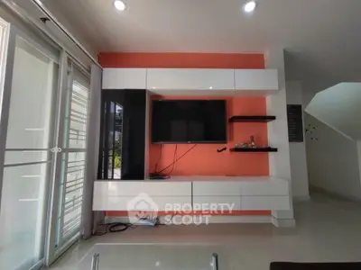 Modern living room with sleek entertainment unit and vibrant orange accent wall.