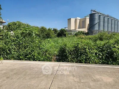Vacant land with lush greenery and industrial backdrop, ideal for development opportunities.