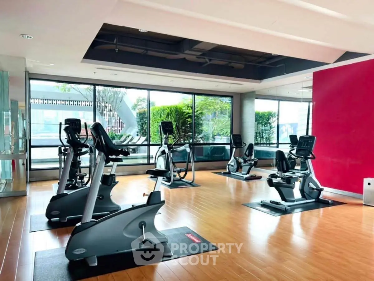 Spacious gym with modern exercise equipment and large windows offering natural light.