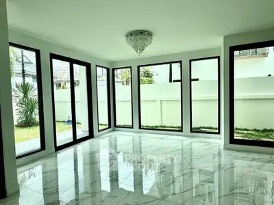Spacious modern living room with large windows and marble flooring, offering abundant natural light and garden views.