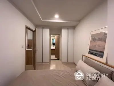 Spacious bedroom with modern minimalist design, featuring a large bed, sleek built-in wardrobes, and a tasteful art piece, leading to an en-suite bathroom.