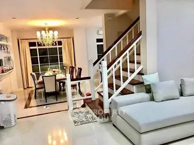 Elegant living room with staircase and dining area, featuring modern furniture and chandelier lighting.