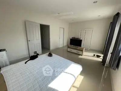 Spacious bedroom with modern decor and natural light, featuring a cozy bed and entertainment setup.