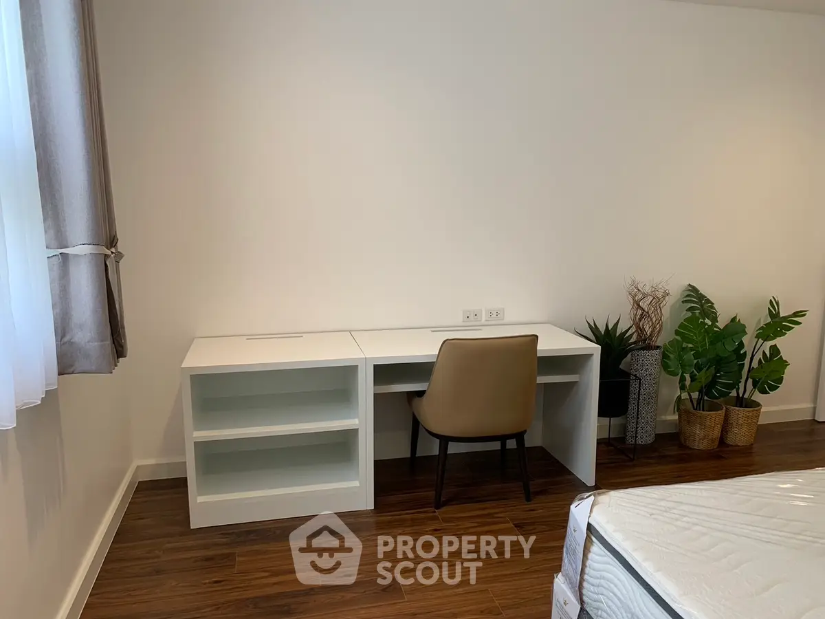 Modern bedroom with sleek desk and chair, hardwood floors, and stylish decor plants.