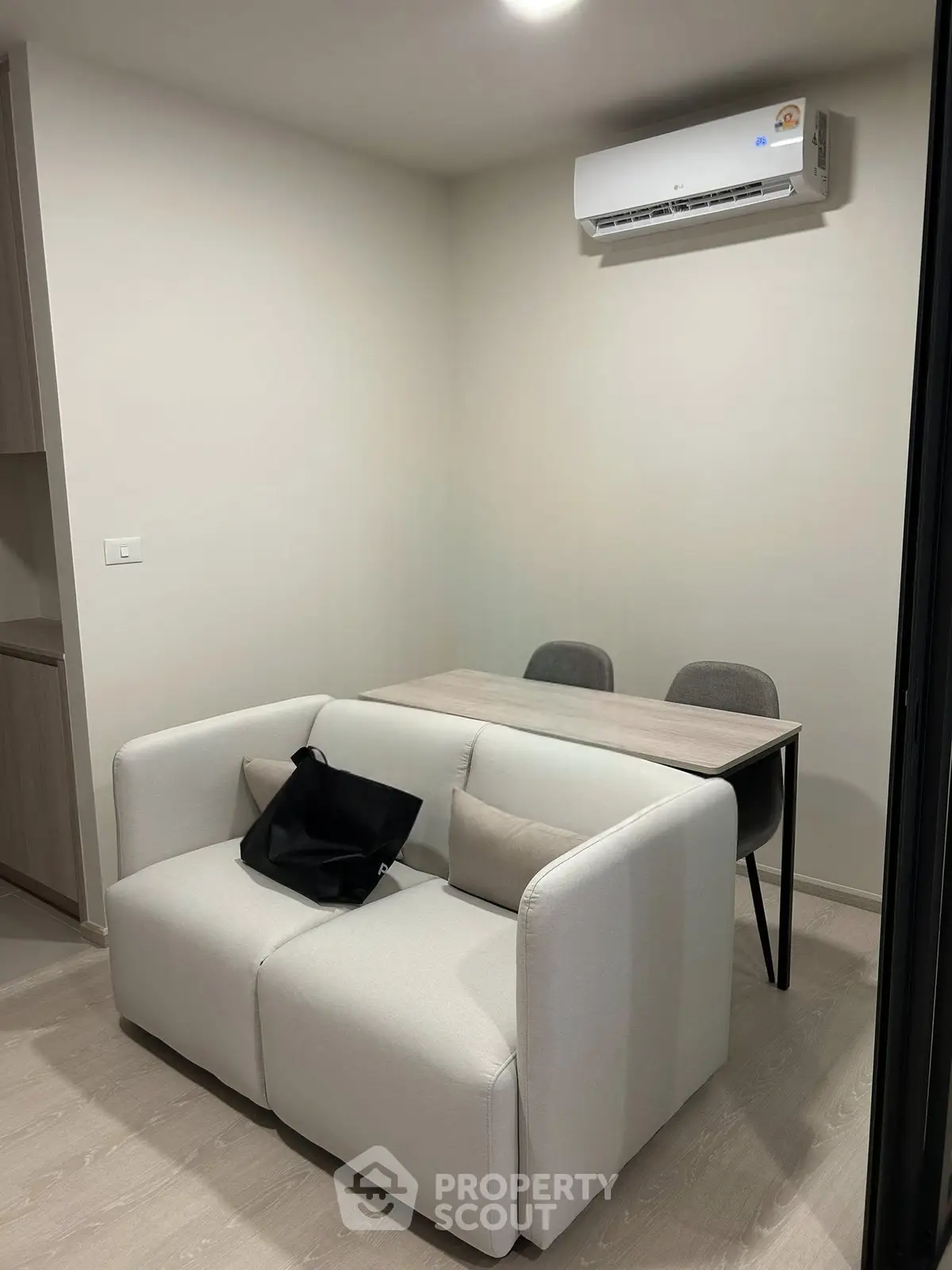 Modern living room with compact sofa and dining table under air conditioning unit.