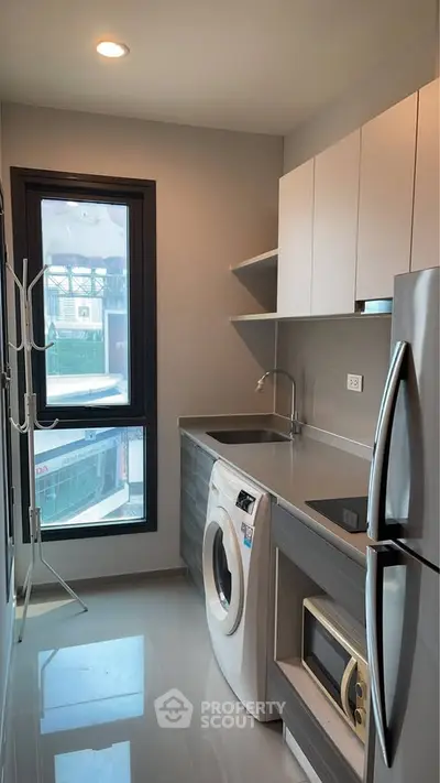 Modern kitchen with sleek cabinets, washing machine, and stainless steel fridge in a compact layout.