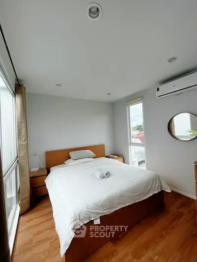 Bright and cozy bedroom with wooden flooring and large windows offering natural light.