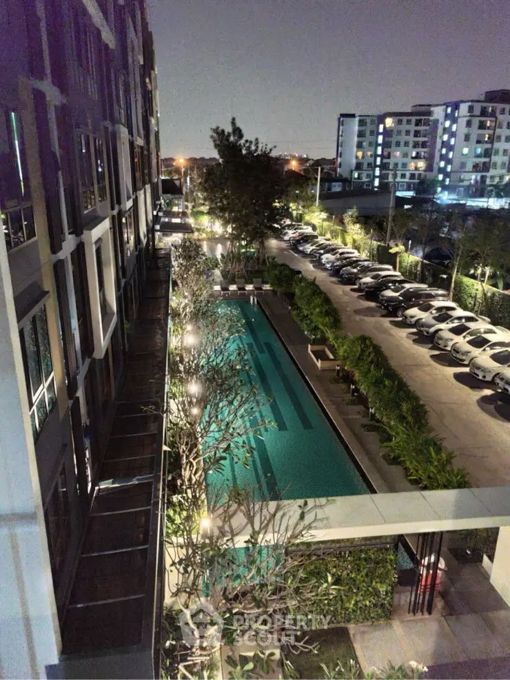Stunning night view of modern apartment complex with illuminated pool and parking area.