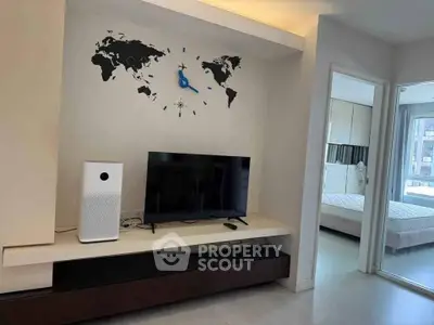 Modern living room with wall clock and TV, adjacent to a bright bedroom with large windows.