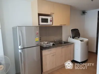 Modern kitchen with fridge, microwave, and washing machine in compact layout.