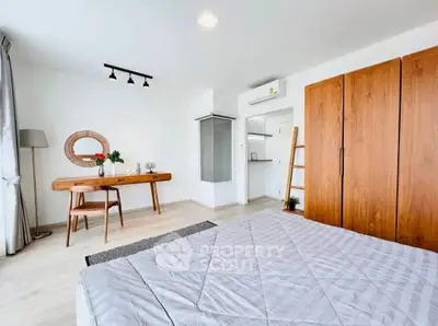 Spacious bedroom with modern decor and natural light, featuring a wooden wardrobe and desk.