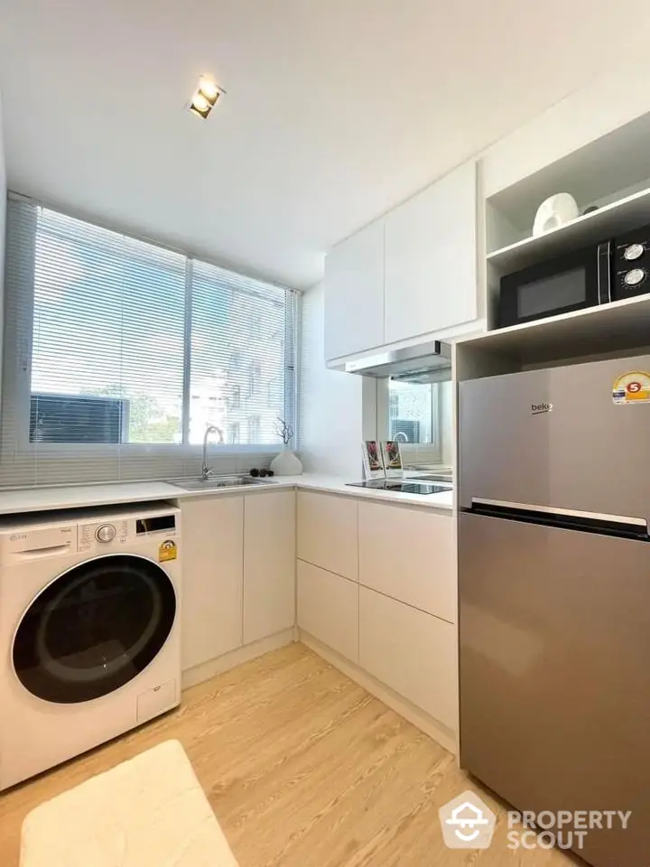 Modern kitchen with sleek appliances and natural light, featuring a washing machine and microwave.