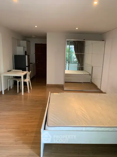Spacious studio apartment with wooden flooring, mirrored wardrobe, and compact kitchen area.