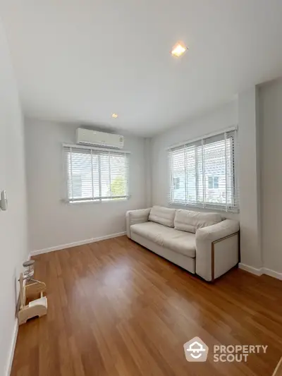 Spacious living room with gleaming hardwood floors, ample natural light from large windows, and a modern, comfortable sofa, perfect for relaxing or entertaining guests.